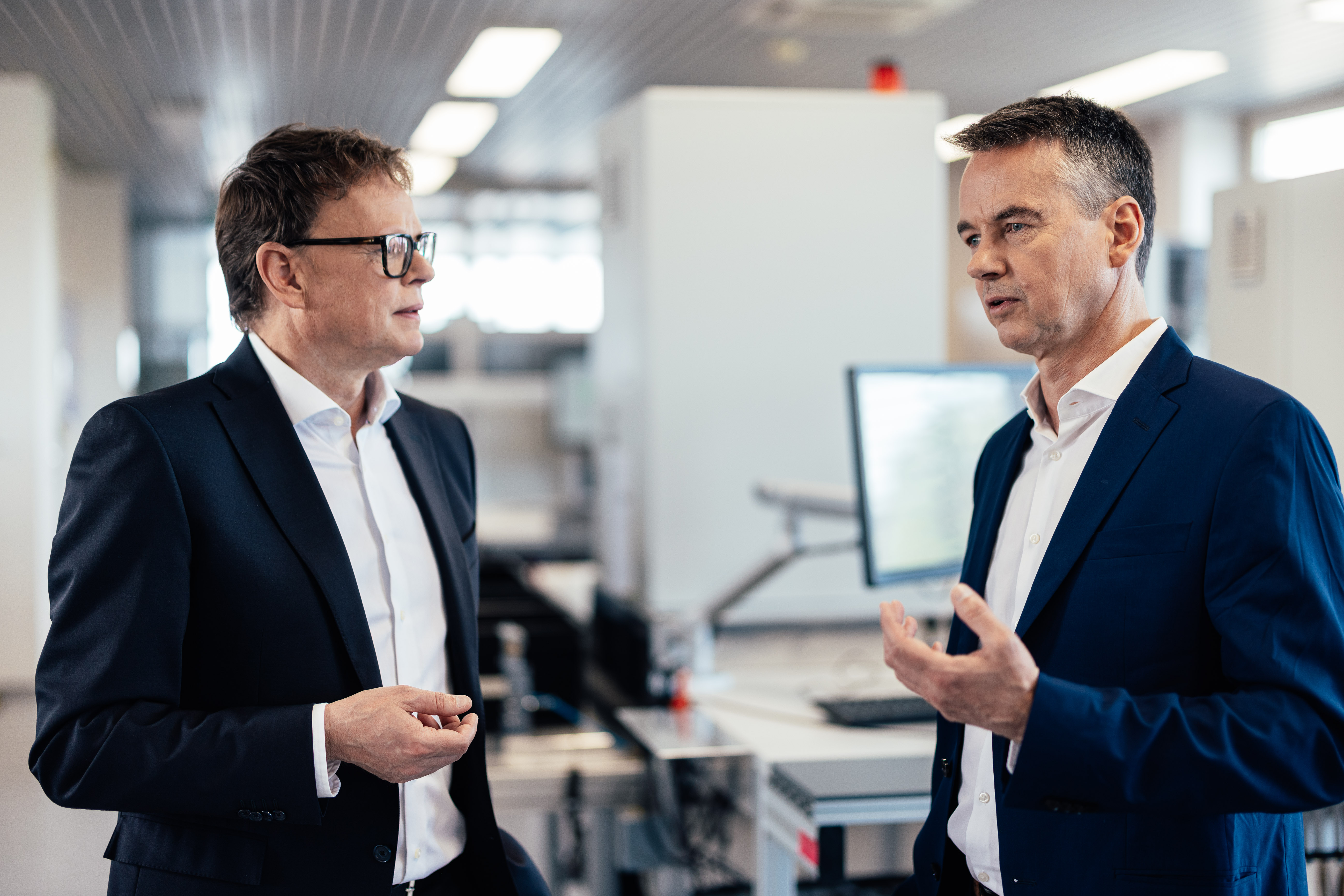 The image shows the Noris managing directors Michael and Florian Schmidmer disussing in a bright white coloured room in the company.