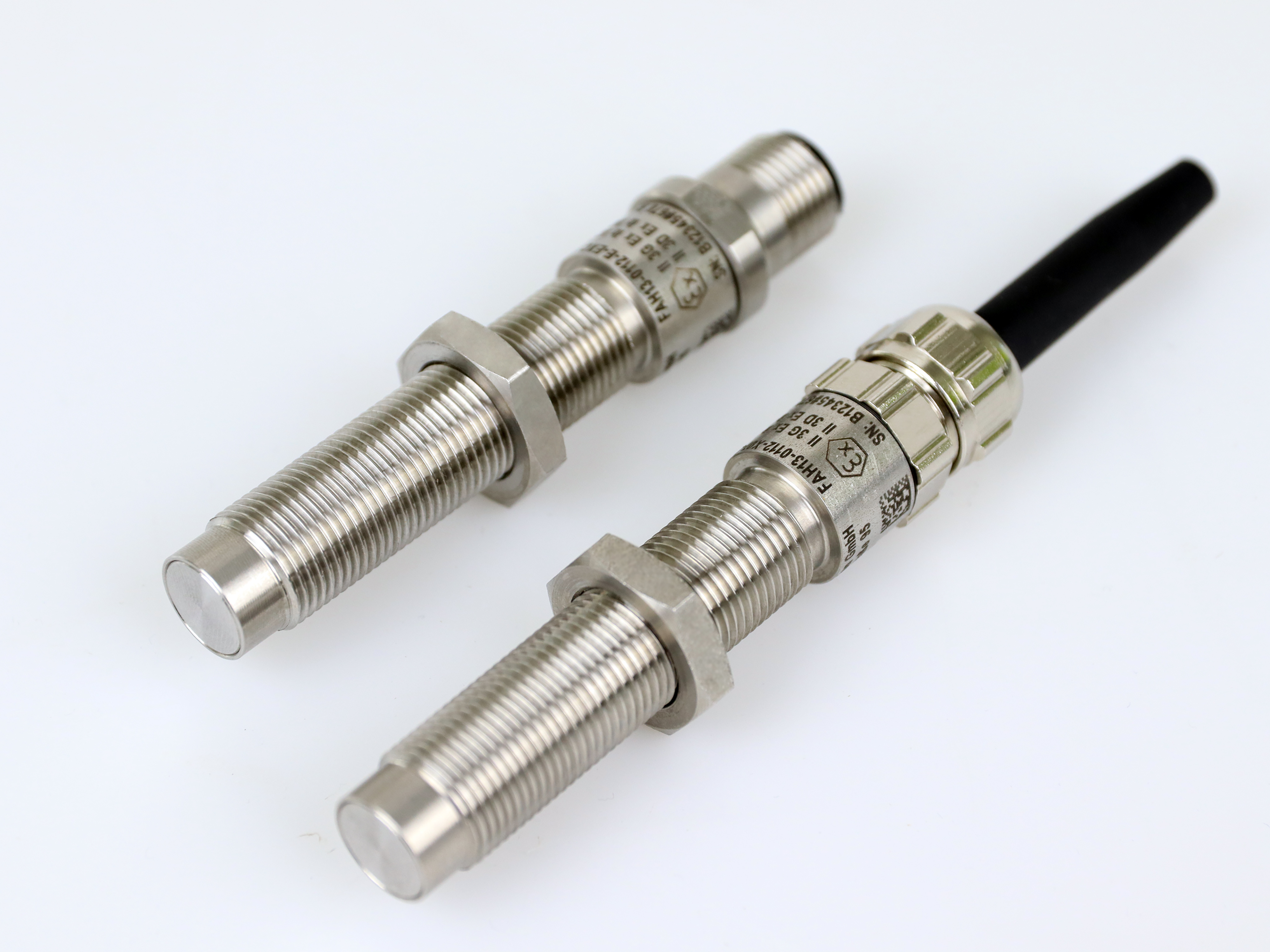 The image shows two threaded stainless steel speed sensors, one with a cable end ond the other witha connector plug laying on a grey background
